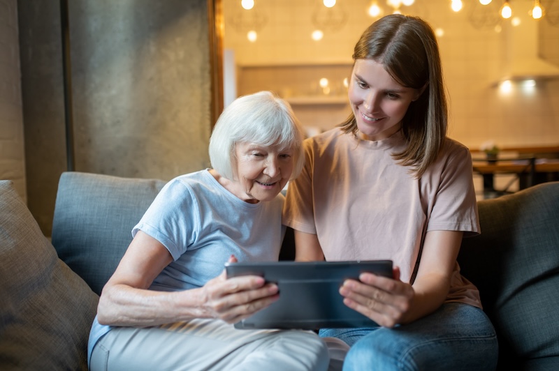 Eine alte und eine junge Mandantin schauen sich auf dem Sofa mit einem Tablet die steuerlichen Ergebnisse an